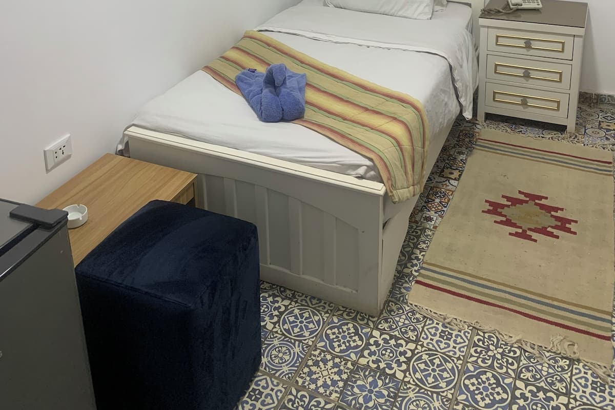 A bedroom with a bed, bedside table, nightstand, and a small desk.