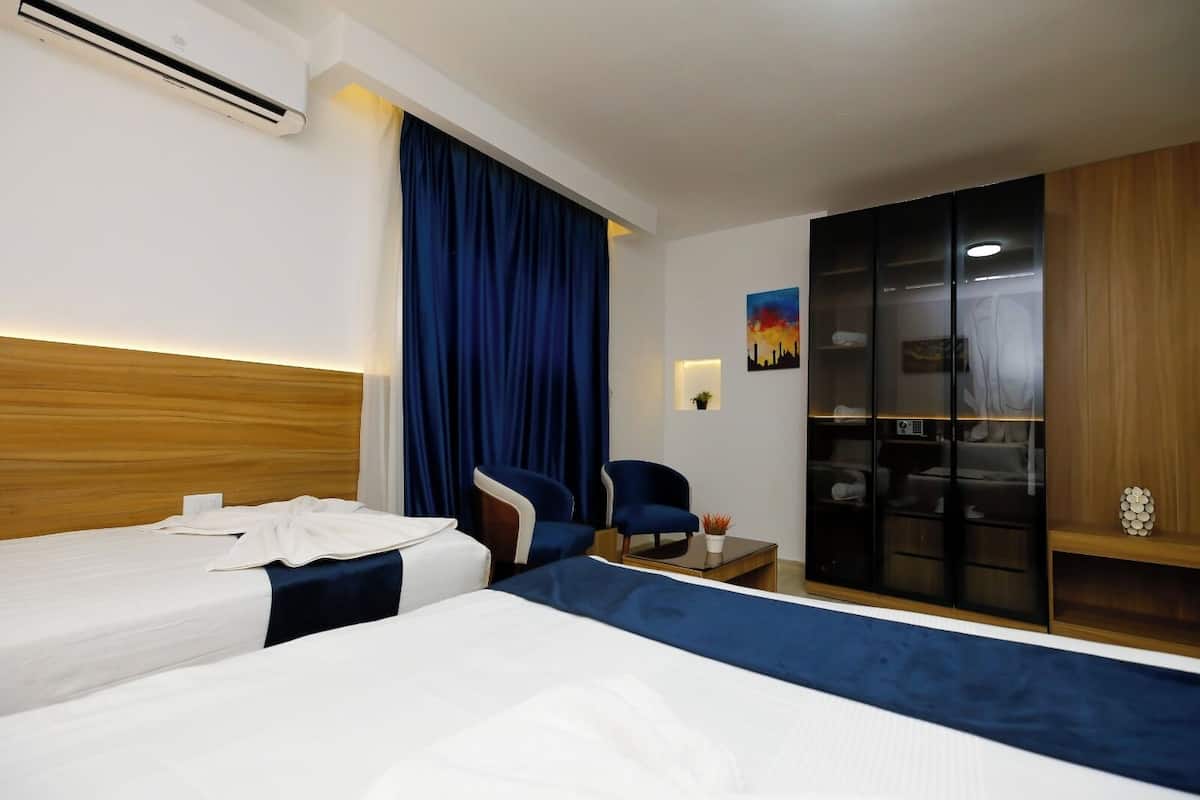 A hotel room with two beds, a desk, a chair, a wardrobe, and a painting on the wall.