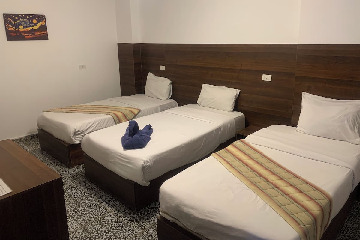 A hotel room with three single beds, a wooden headboard, a small table, and a patterned floor.