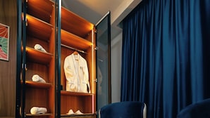 A hotel room with a wooden wardrobe, a blue armchair, a small table with a plant, and a blue curtain.