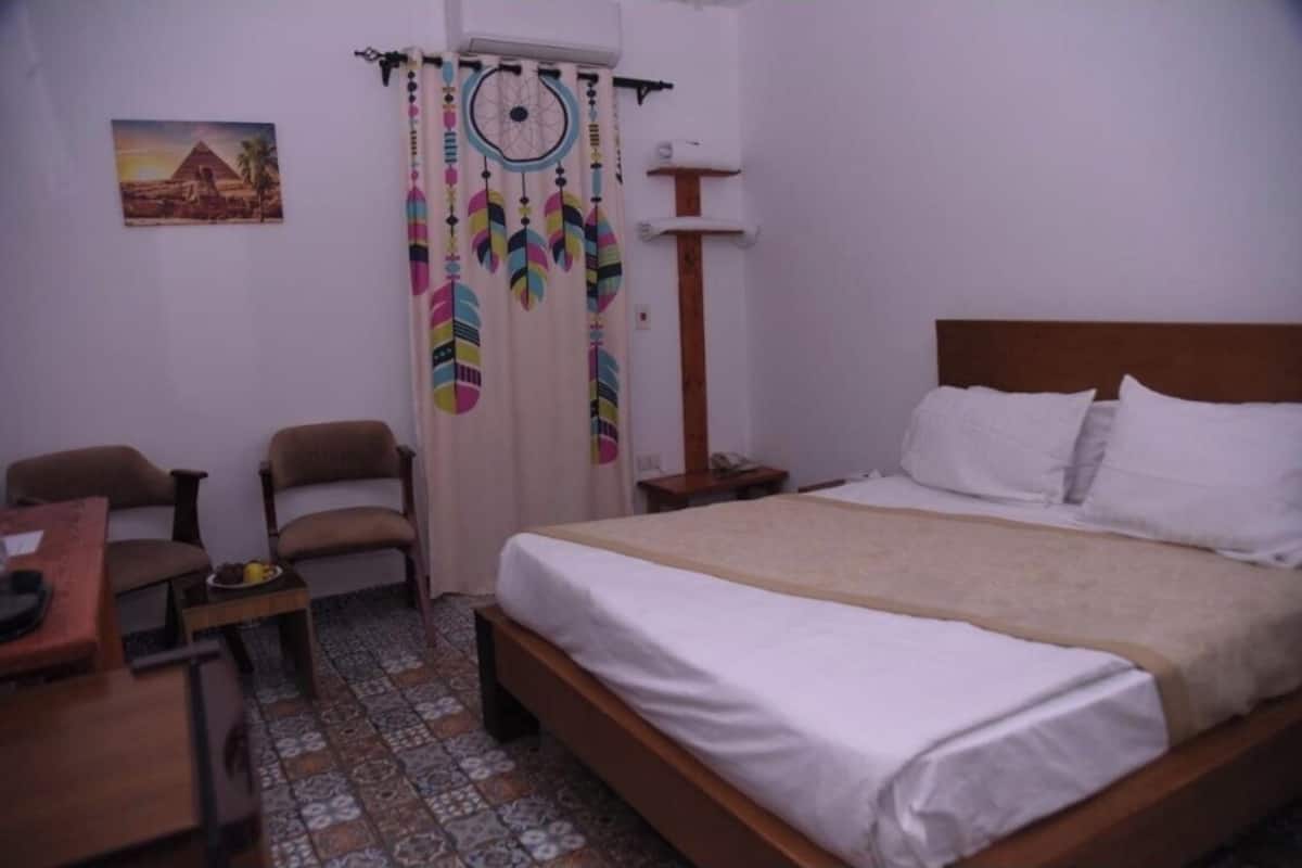 A bedroom with a bed, two chairs, a small table, a nightstand, and a dreamcatcher.