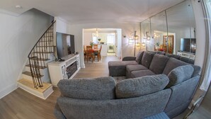 A modern living room with a grey sectional sofa, a TV on a white stand, and a staircase with wooden steps. - Family Home-Sleeps 8-Spacious 3BR-Free Parking-8 Min to PHL (Sharon Hill)