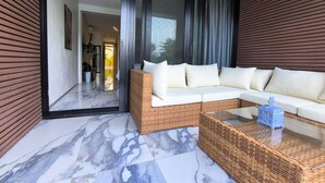 A modern living area with a wicker sofa, a glass door leading to a kitchen, and a marble floor.