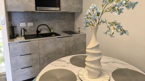 A modern kitchen with grey cabinets, a built-in microwave, a sink with a black faucet, and a vase with blue flowers on a round table with a marble pattern.