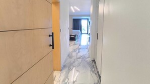 A hallway with wooden cabinets, a marble floor, and a bed in the distance.