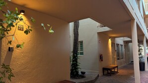 An outdoor corridor with a wooden bench, a fire extinguisher, and a potted plant.