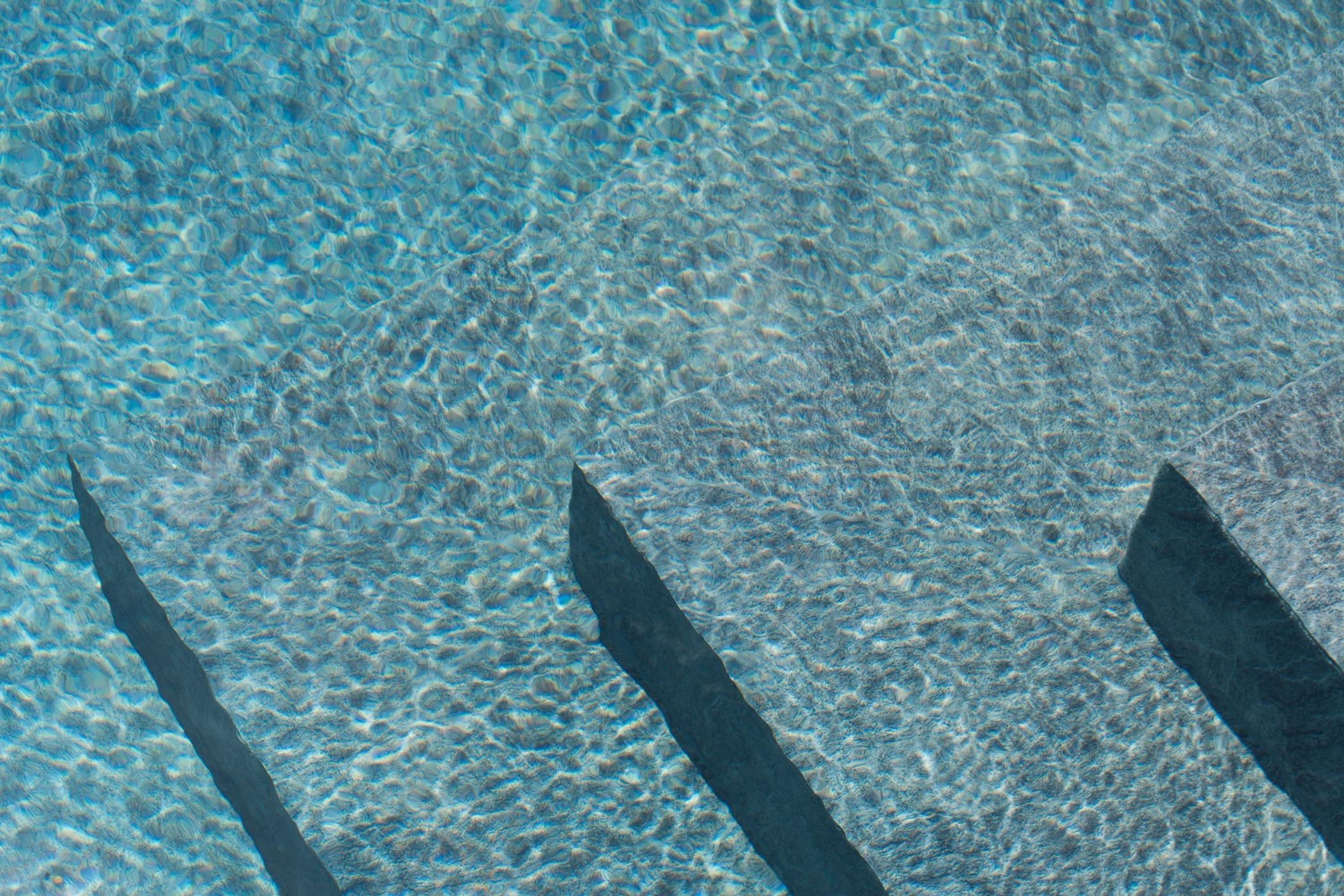 A clear view of a swimming pool with visible water clarity and shadows cast by objects.