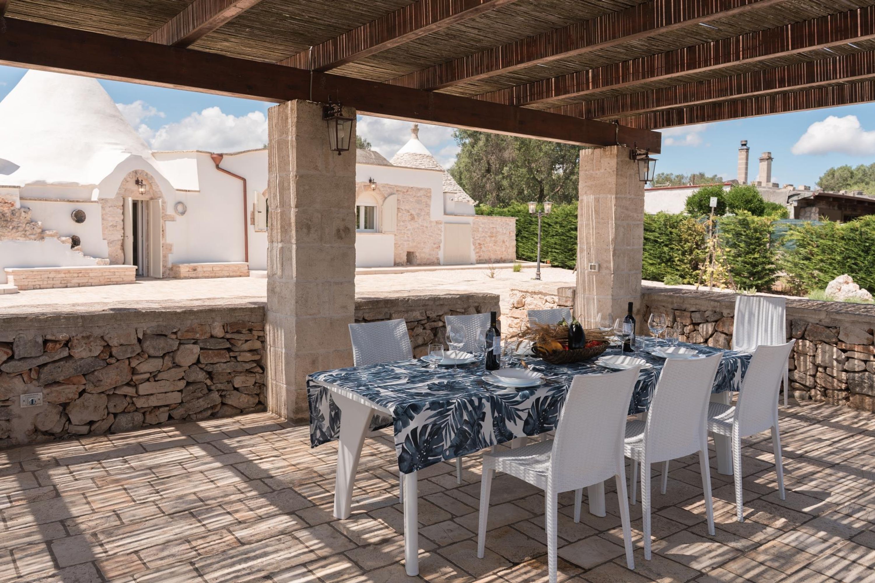 Une terrasse extérieure avec une table dressée pour le repas, des murs en pierre et une vue sur un bâtiment blanc doté de coupoles.