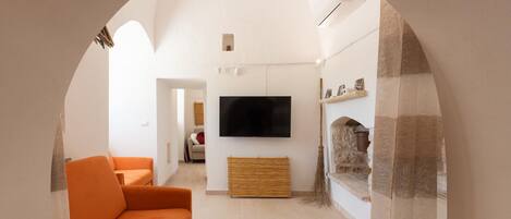 A modern living room with a large flat-screen TV, orange sofas, and a stone fireplace.