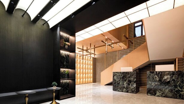 Un hall d’entrée moderne avec un escalier, un comptoir de réception en marbre et des meubles noirs et dorés.