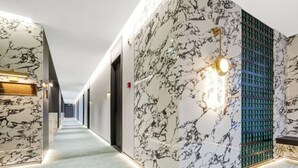 Un couloir d’hôtel moderne avec des murs en marbre, une moquette à motifs et un long couloir bordé de portes.