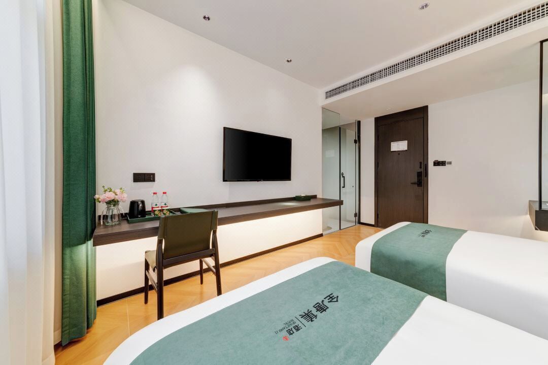 A hotel room with two beds, a desk with a flat-screen TV, a chair, and a small table with a vase of flowers.