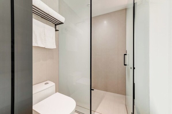 A modern bathroom with a glass shower enclosure, a white toilet, and a towel rack.