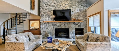 A living room with a stone fireplace, a flat-screen TV, and a staircase.