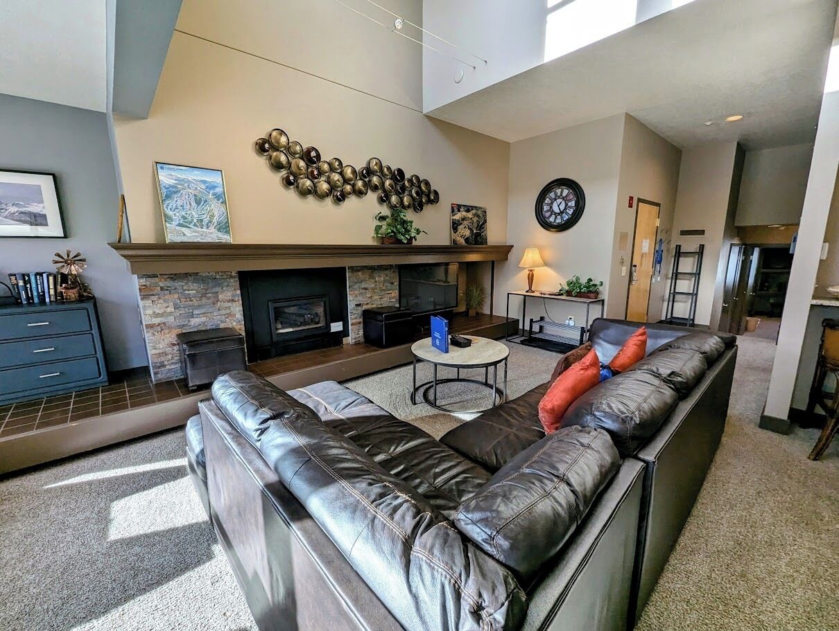 A spacious living room with a large black leather sofa, a fireplace, a coffee table, and a dining area.