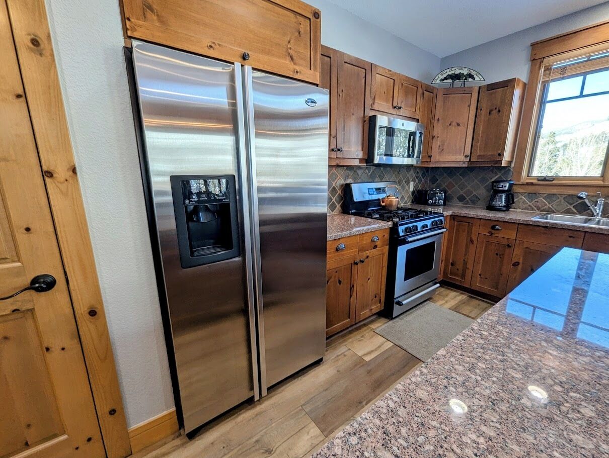 A kitchen with wooden cabinets, stainless steel appliances, granite countertops, and a window.