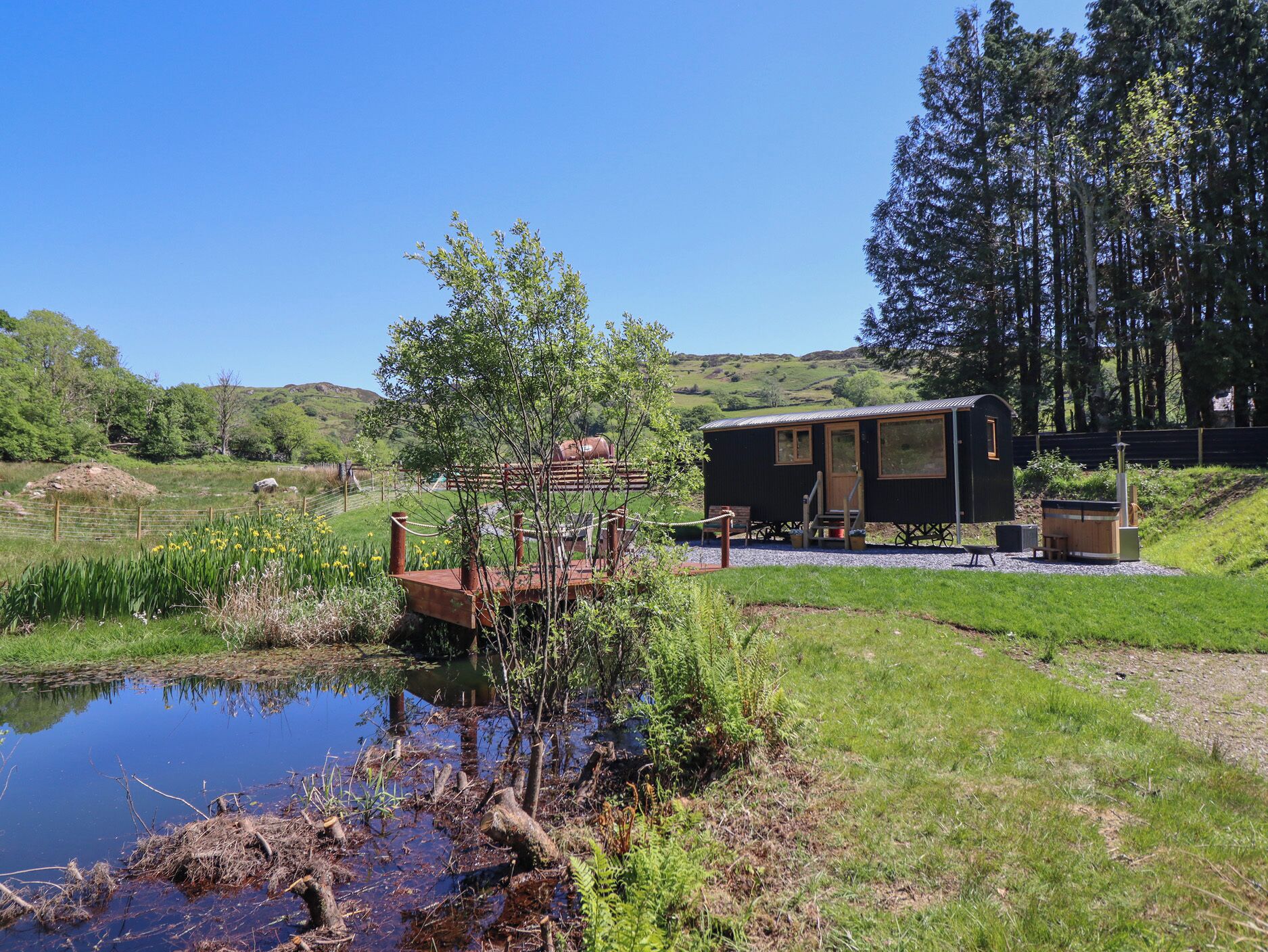 A rustic cabin with a small deck and a pond in a lush, green landscape.