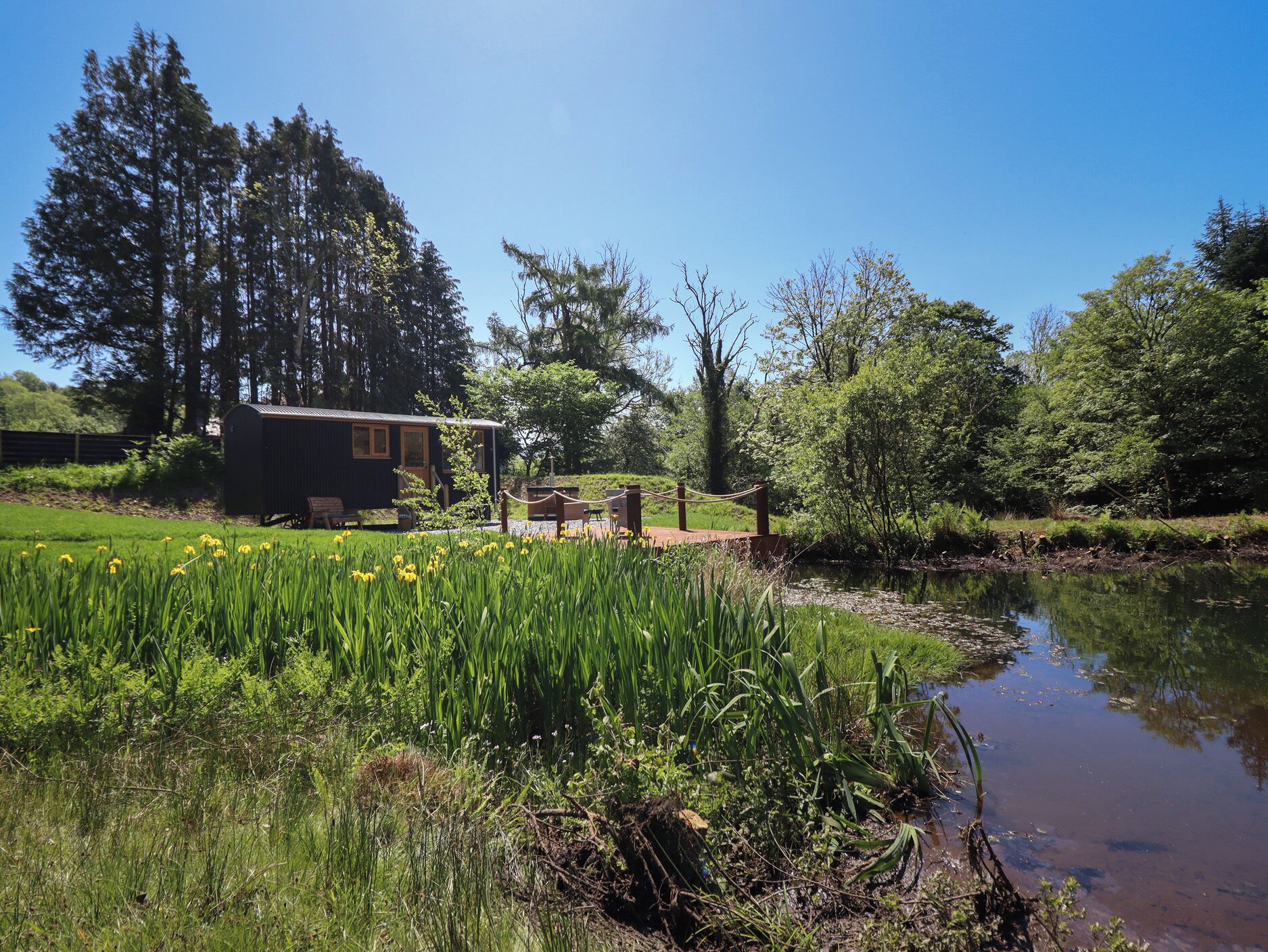 Eine rustikale Holzhütte mit einer kleinen Terrasse, umgeben von üppigem Grün und einem Teich.