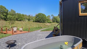 Ein Whirlpool mit einer Holzterrasse und Stühlen, umgeben von einem Kiesweg und einem eingezäunten Bereich mit Bäumen.