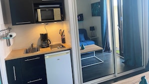A compact kitchen with a microwave, coffee maker, and a dishwasher. There is a seating area with a blue chair and a small table. - 2-person studio with sea view and pool in Porticcio residence. Corsica. (Grosseto-Prugna)