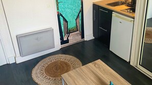 A compact kitchen with a sink, stove, and microwave. A small dining table with a blue vase is in the center. - 2-person studio with sea view and pool in Porticcio residence. Corsica. (Grosseto-Prugna)