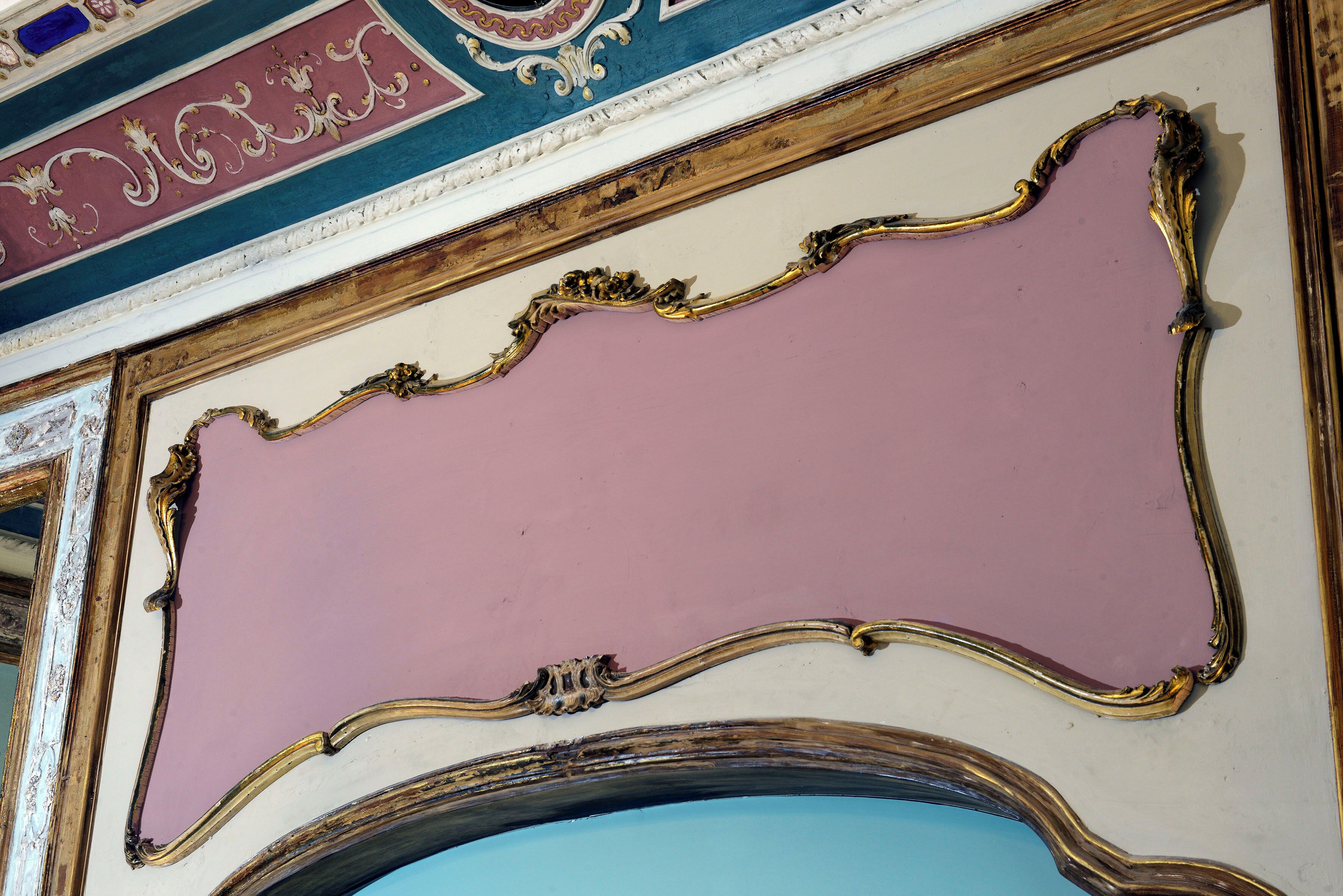 A room with ornate gold-framed mirrors and a pink wall.