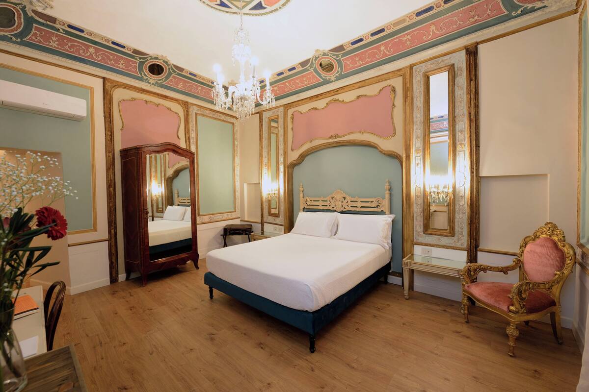 A bedroom with a large bed, a vanity with a mirror, a chair, and a chandelier.