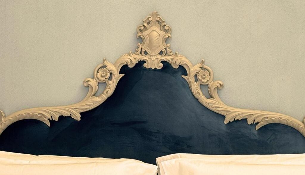 Una cama con cabecera oscura y paneles laterales ornamentados de color claro.