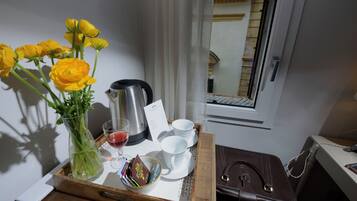 A tray with a vase of yellow flowers, a coffee pot, and white cups and saucers on a table.