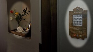 Una puerta con cerradura electrónica y teclado, con la etiqueta '6 AFFRESCO', y una pequeña ventana con un arreglo floral.