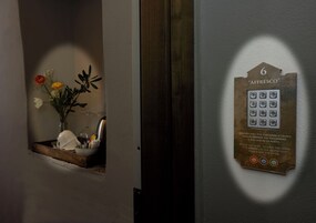 Una puerta con cerradura electrónica y teclado, con la etiqueta '6 AFFRESCO', y una pequeña ventana con un arreglo floral.