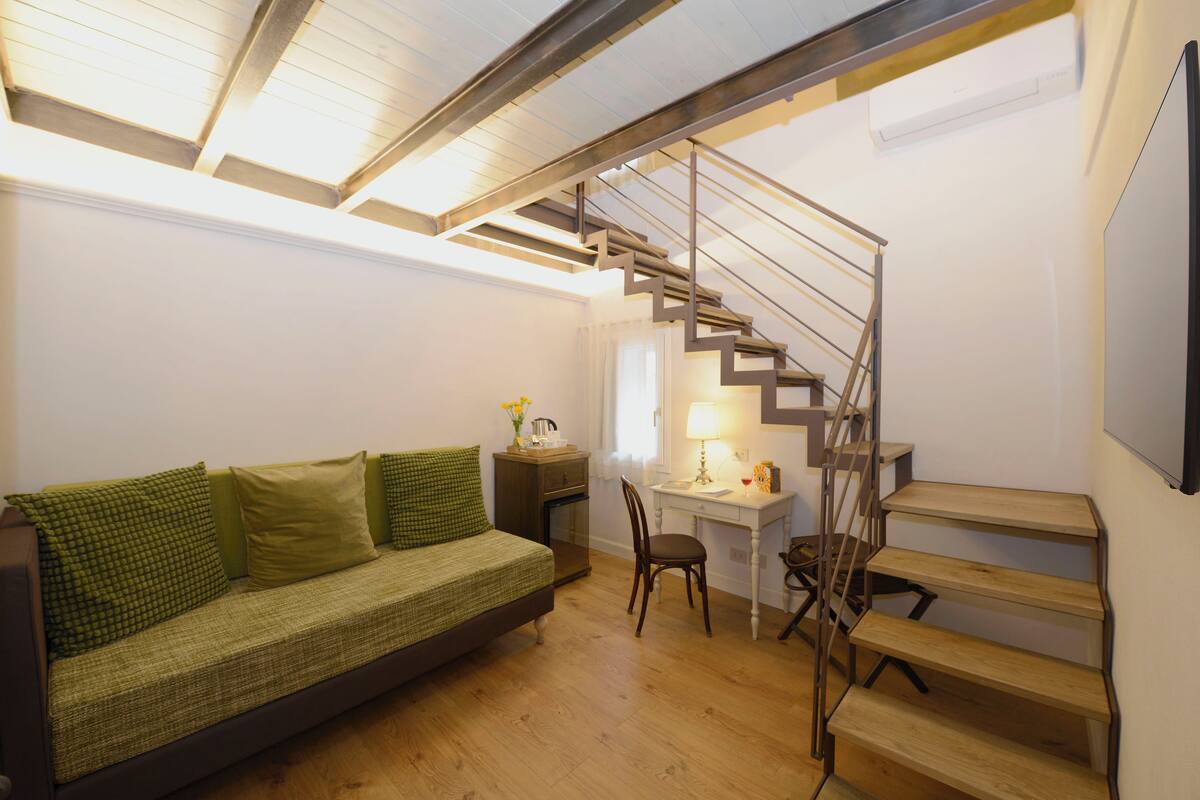 A room with a wooden staircase, a green sofa, a desk with a lamp, and a chair.