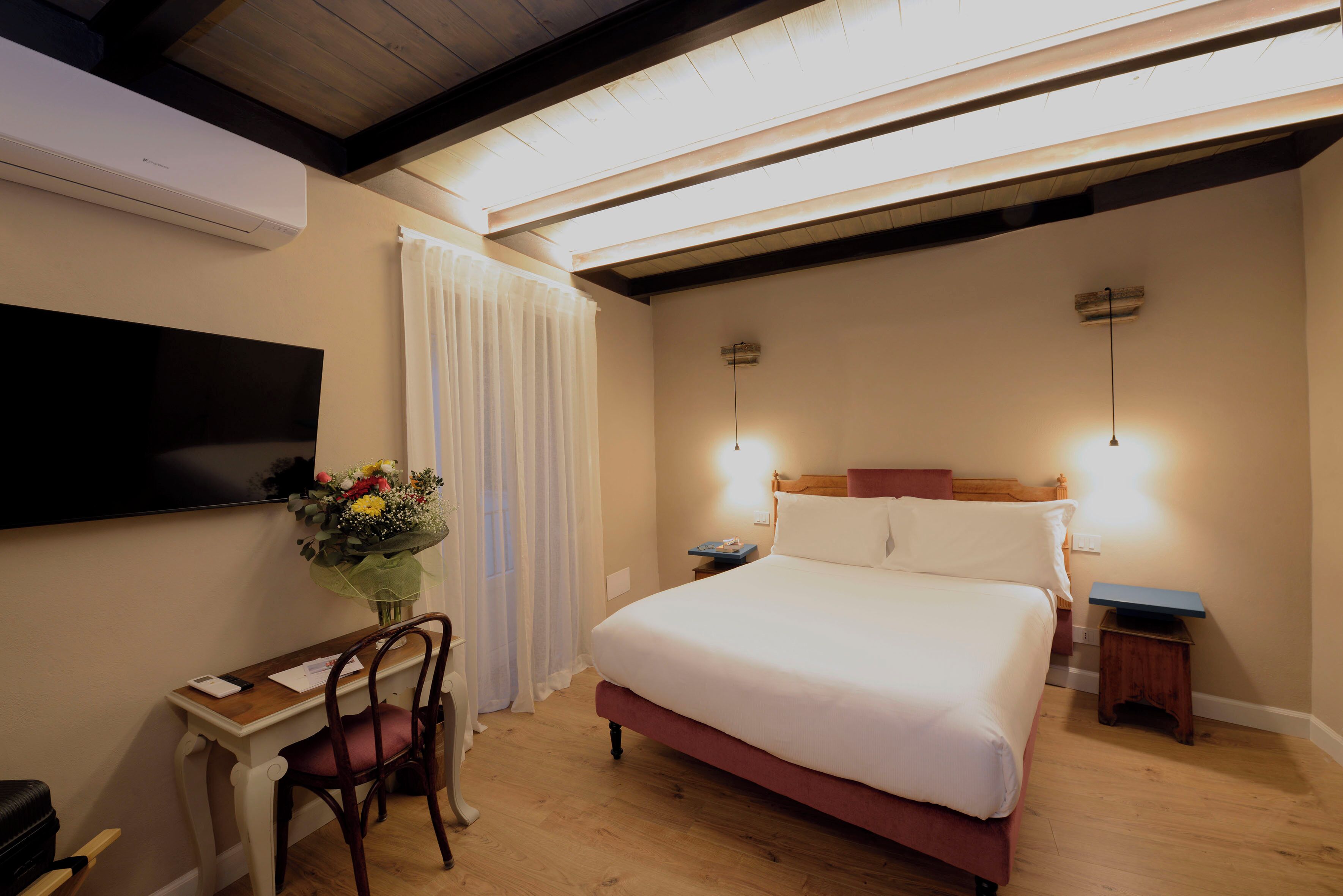 Un dormitorio con cama, escritorio, silla, televisión y mesita de noche con lámpara.