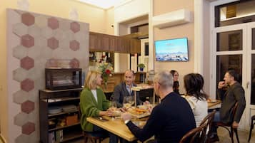 A group of people dining in a room with a hexagonal patterned wall, a television, and a wooden table.