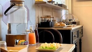 Una cocina con cafetera, vaso de jugo de naranja y un plato de fruta.
