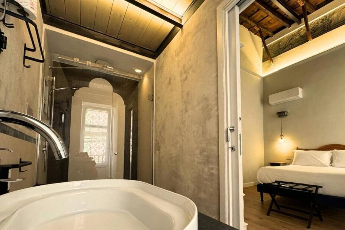 A bathroom with a bathtub, a shower, and a door leading to a bedroom with a bed and bedside table.