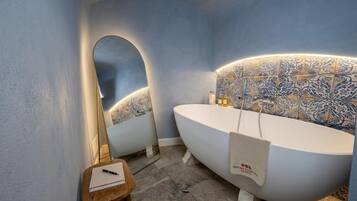 A modern bathroom with a freestanding bathtub, a vanity with a mirror, and a small wooden stool.