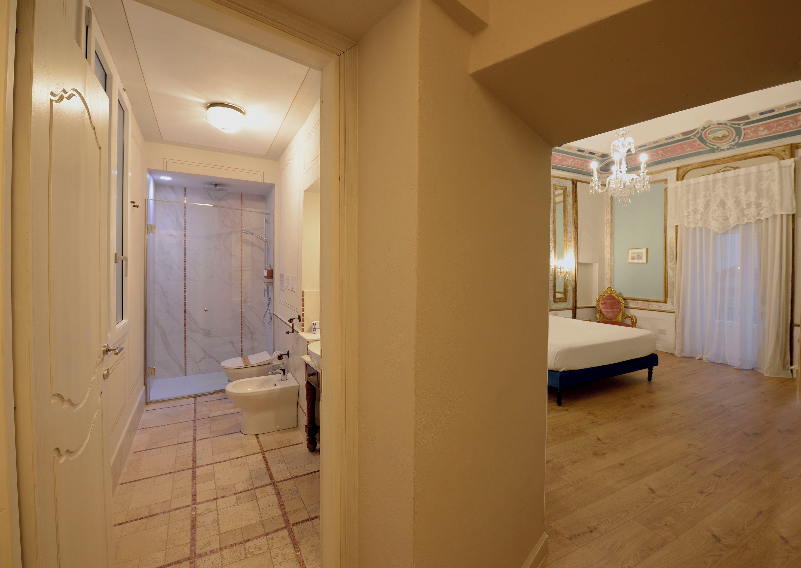 A hotel room with a bathroom, a bed, and a chandelier.