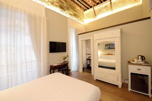 Habitación de hotel con una cama grande, un escritorio con silla, televisor, armario y una pequeña kitchenette.