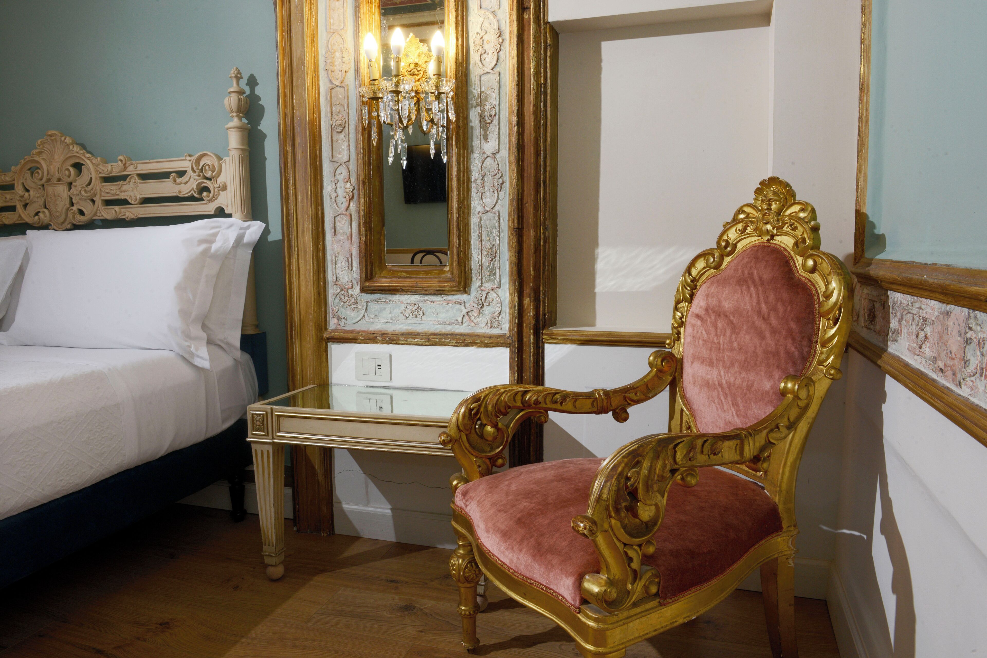A room with a bed, a vanity with a mirror, and an ornate chair.