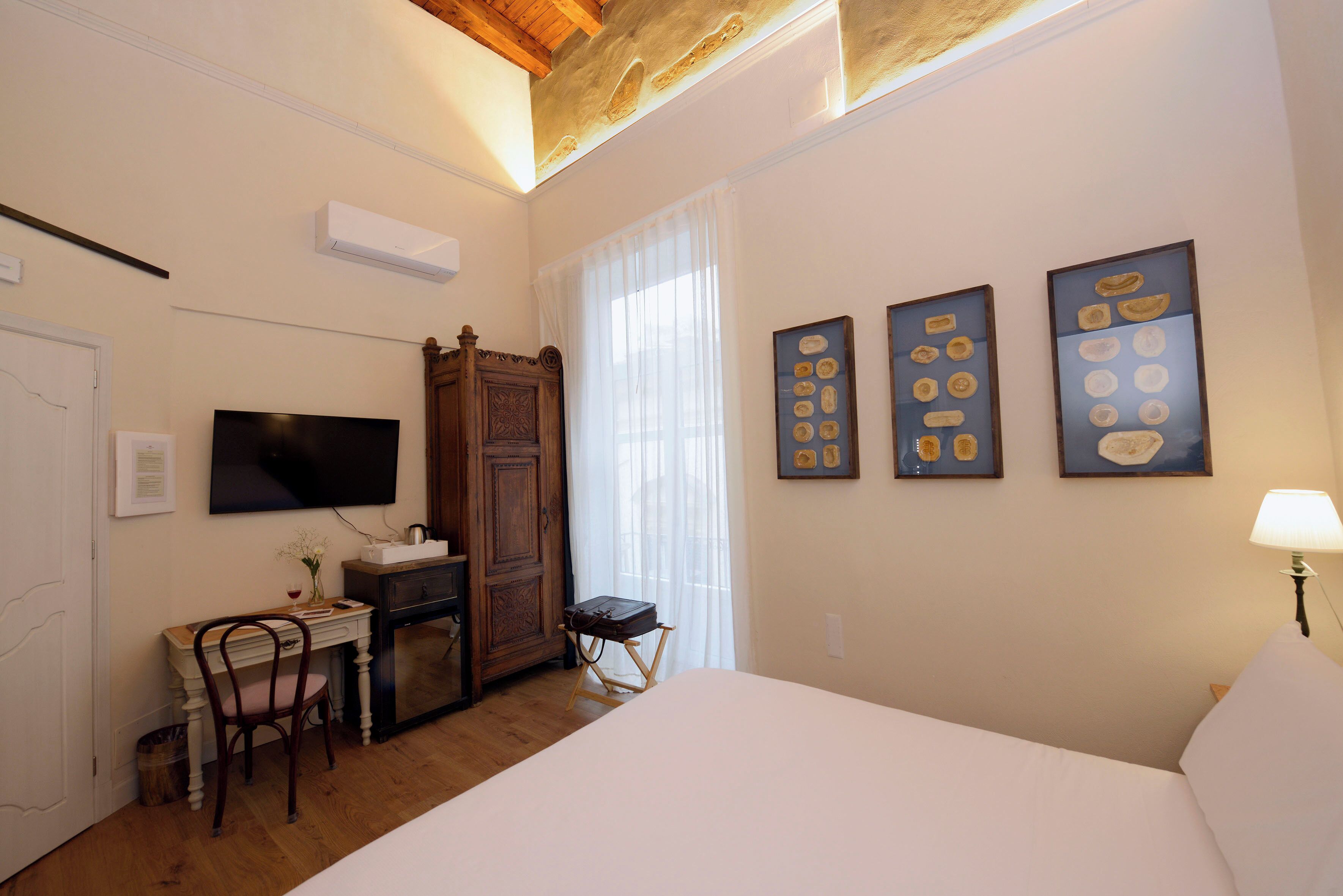 Une chambre d’hôtel comprenant un lit, un bureau avec une chaise, une télévision, une armoire et des œuvres d’art accrochées au mur.