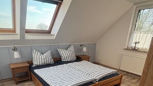 A bedroom with a wooden bed, a nightstand, a window with a view, and a radiator. - Vacation home Küstennebel directly by the sea (Butjadingen)