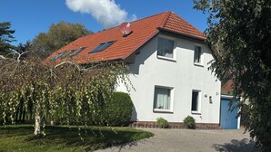 A two-story house with a red-tiled roof, white walls, and a blue garage door. - Vacation home Küstennebel directly by the sea (Butjadingen)