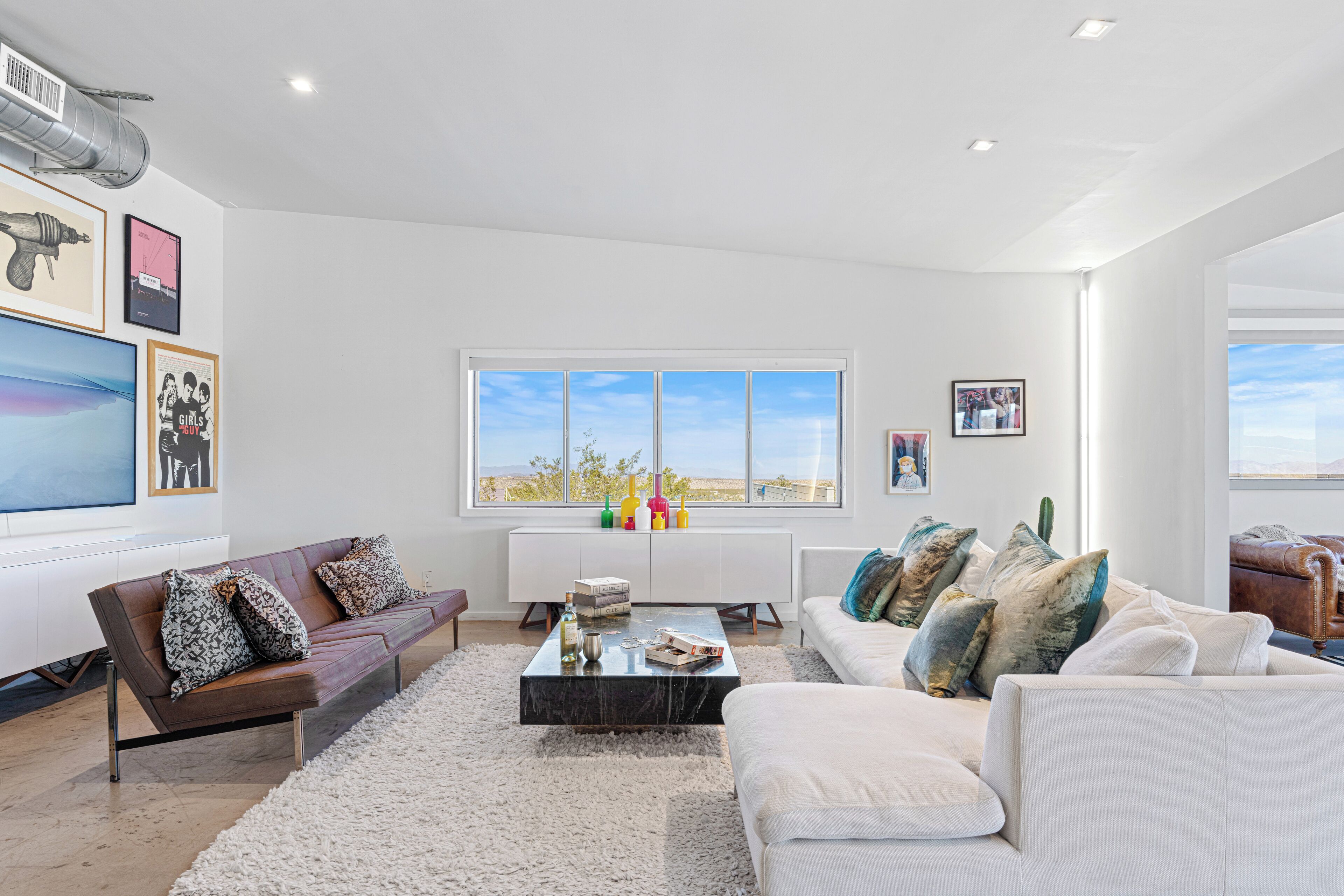 A modern living room with a large window, a white sofa, a brown leather sofa, and a marble coffee table.