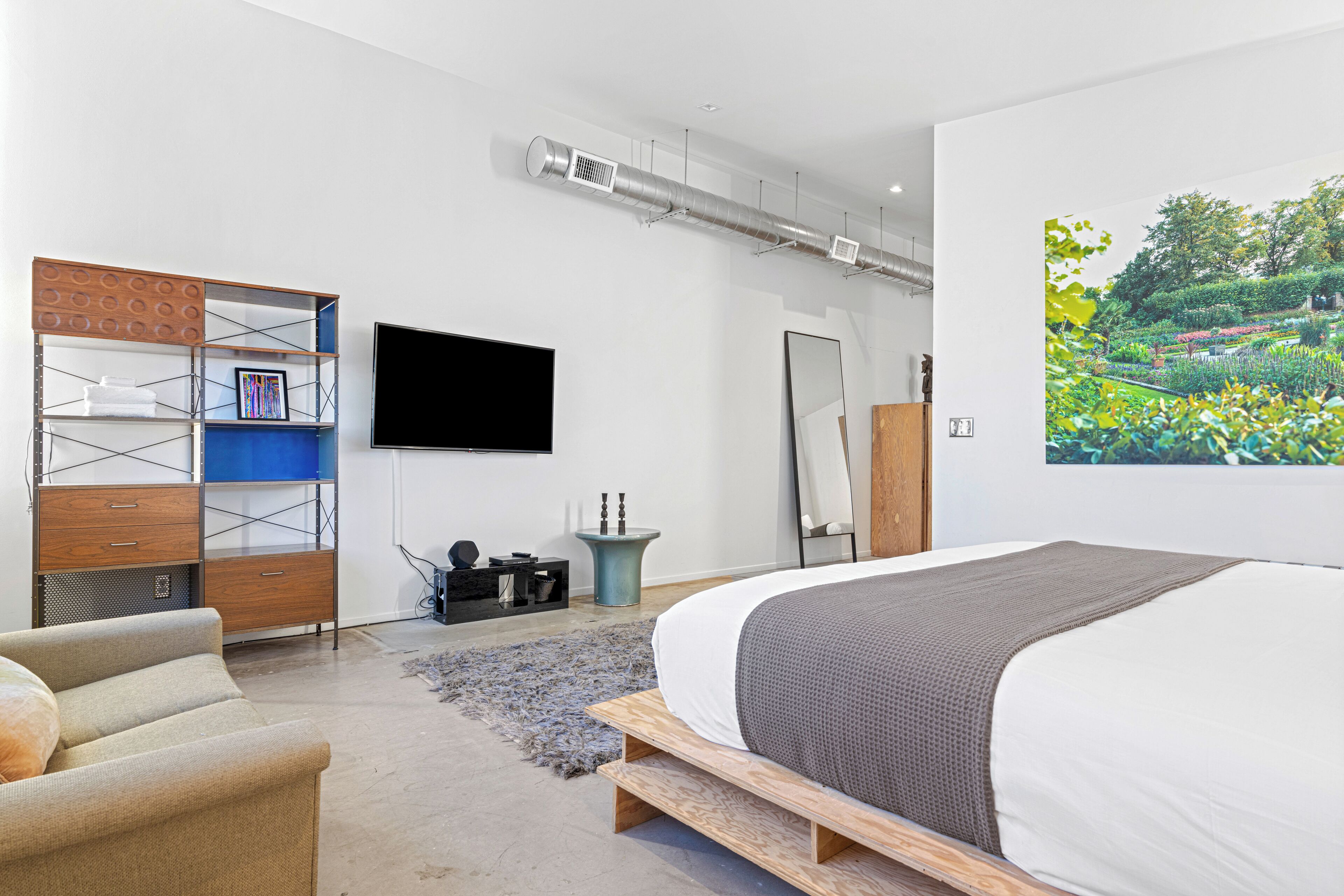 A modern bedroom with a large bed, a TV, a painting, and a built-in shelving unit.