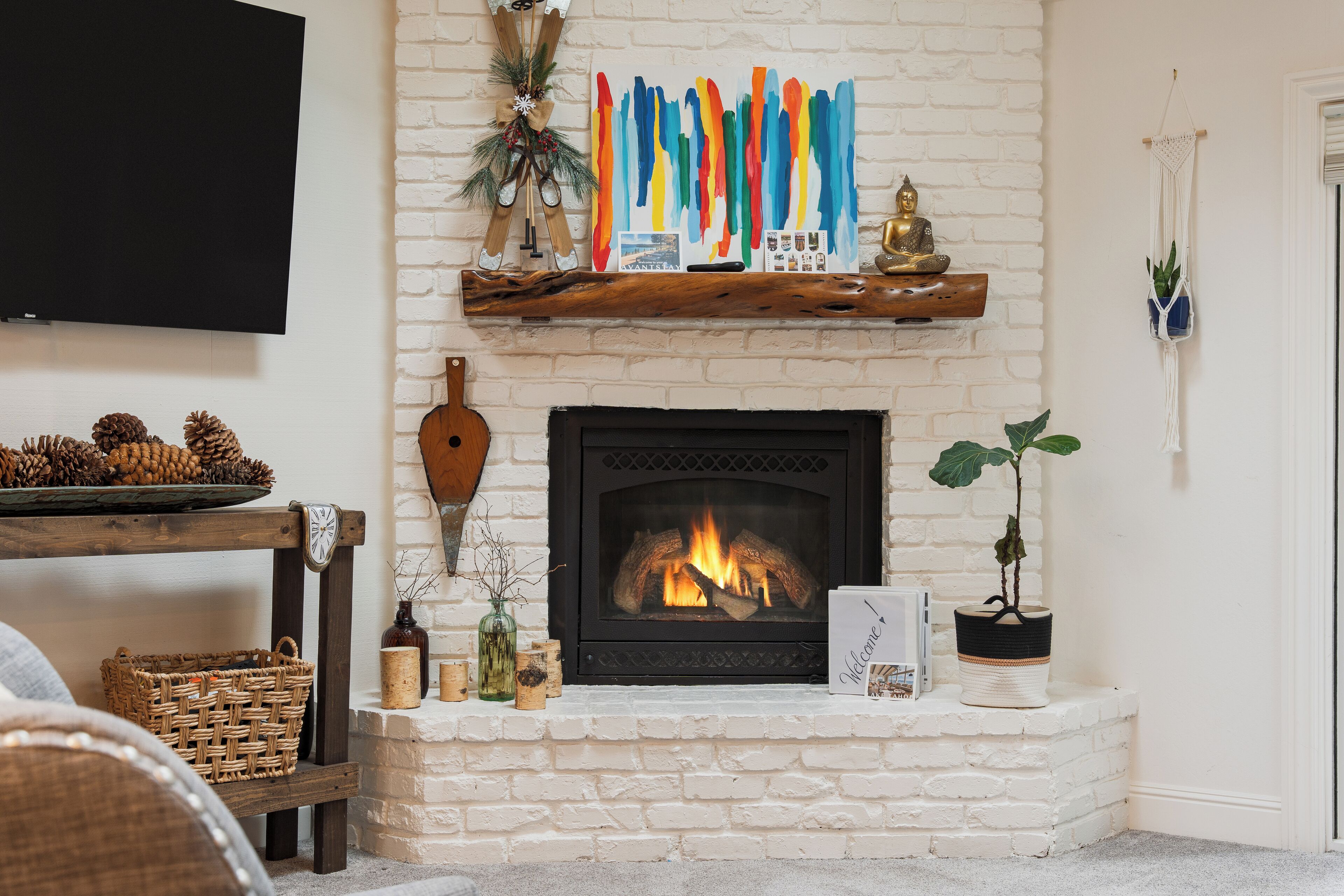 A fireplace with a fire, a television mounted on the wall, and a shelf with decorative items.