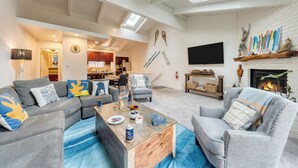 A spacious living room with a fireplace, a dining area, and a kitchen in the background.