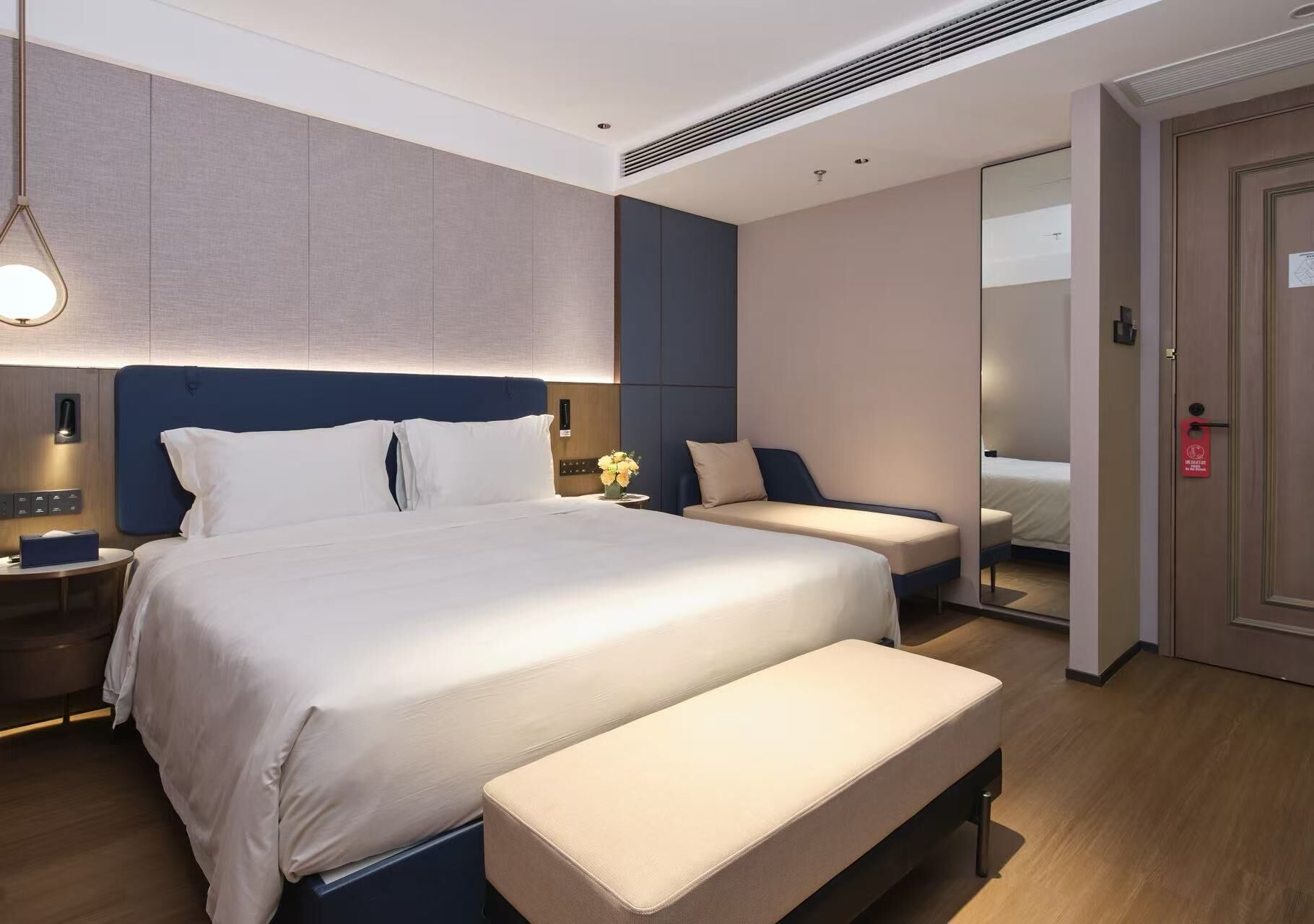 Ein modernes Hotelzimmer mit einem großen Bett, einer Bank, einem Nachttisch und einem Spiegel.