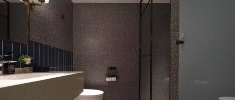 A modern bathroom with a granite countertop, a white toilet, and a glass shower enclosure.