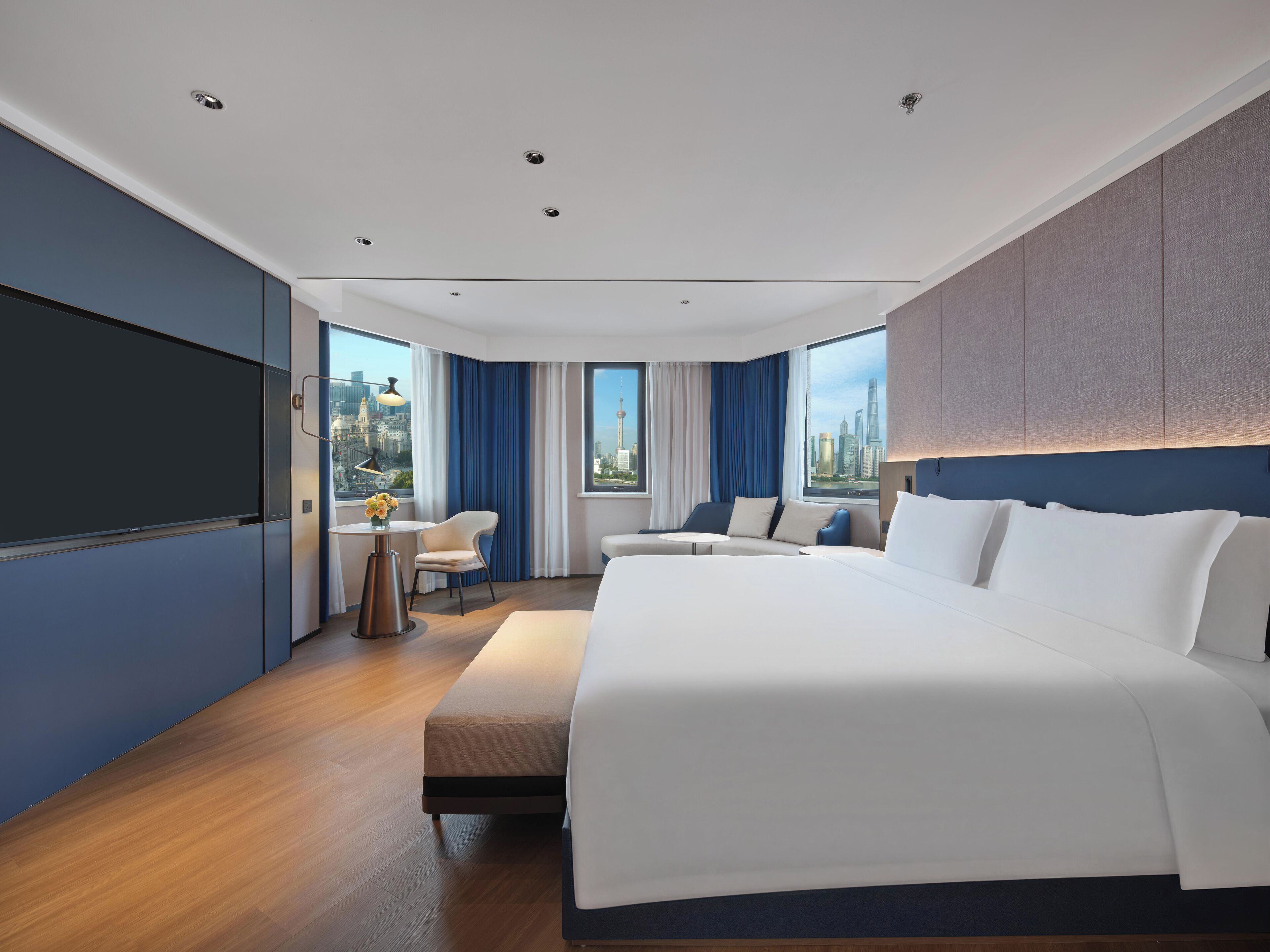 A modern hotel room with a large bed, a seating area, and a city view.